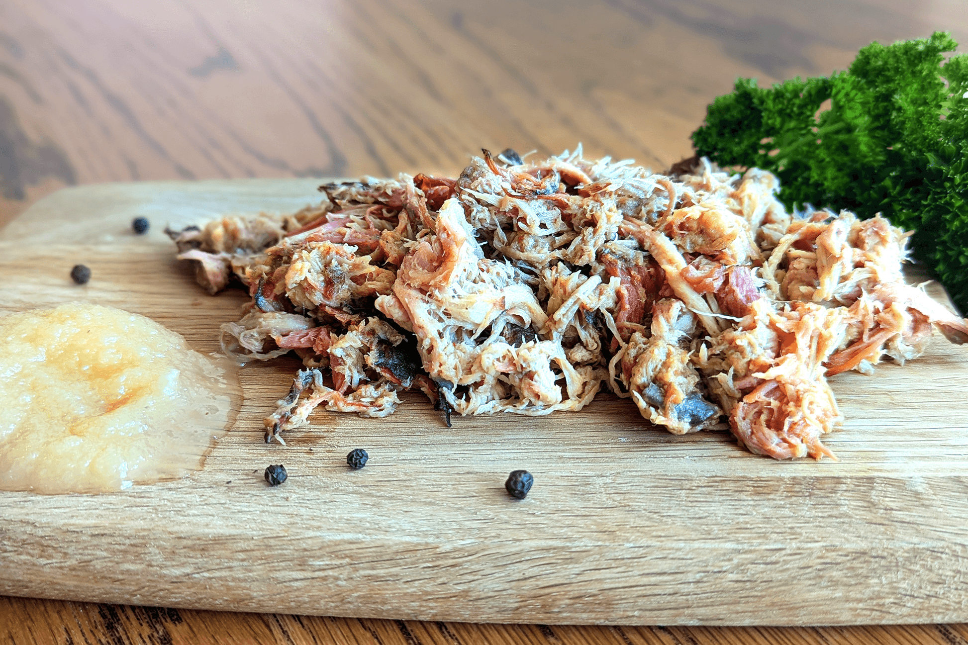 Shredded low and slow pulled pork stacked on wooden chopping board with apple sauce